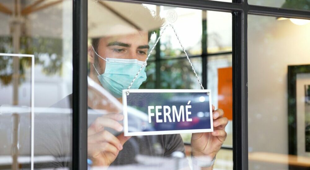 Homme portant un masque sanitaire posant une étiquette "fermé" sur la porte de son commerce