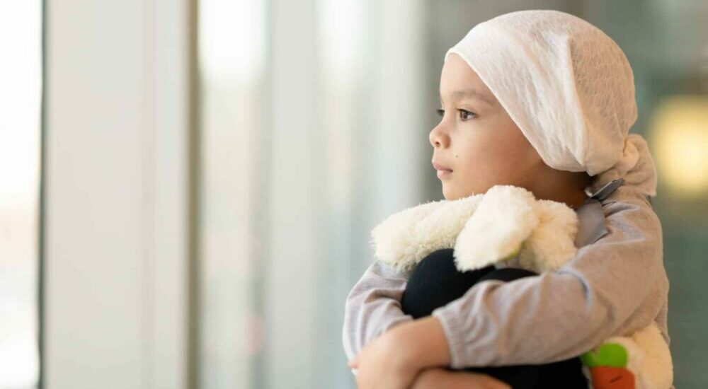 Un jeune enfant atteint d'un cancer tient une peluche le regard dans le vague