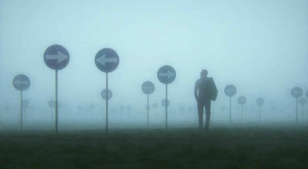 Homme dans la brume au milieu d'un champ de panneau indiquant des directions différentes